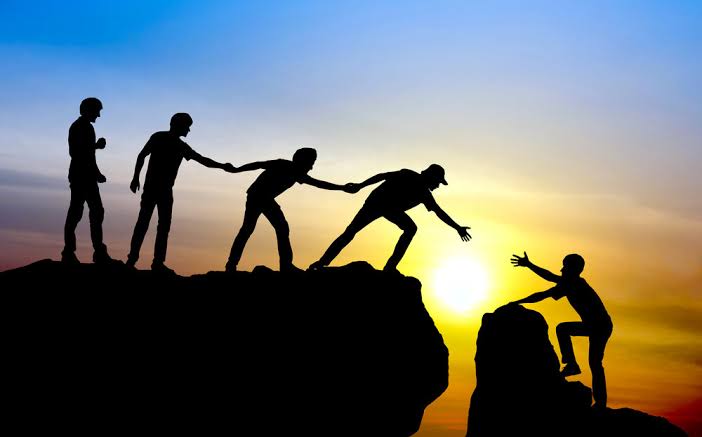 Hikers helping each other up to a mountain summit